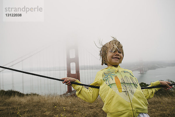 Mädchen lehnt bei nebligem Wetter am Kabel gegen die Golden Gate Bridge