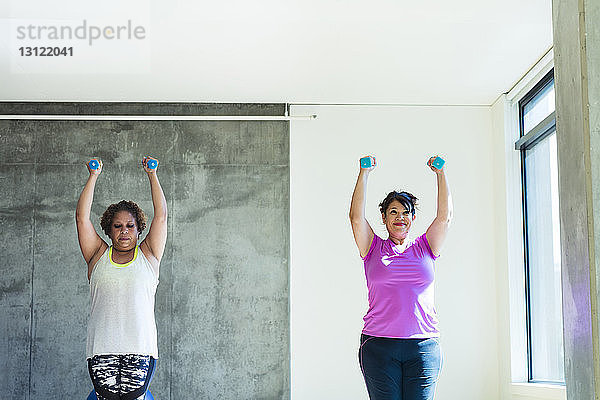 Freundinnen mit Hanteln beim Üben an der Wand im Yogastudio