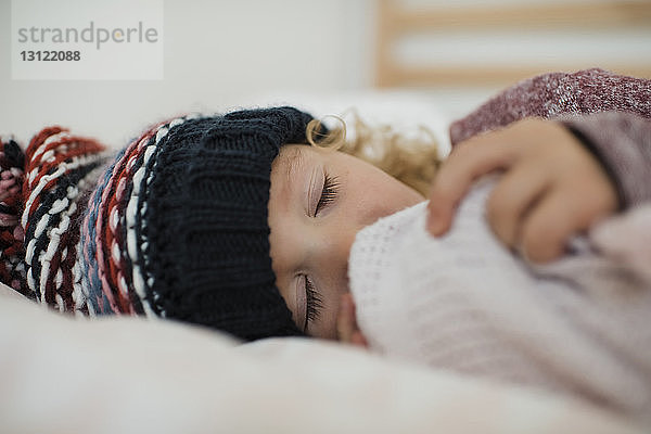 Nahaufnahme eines süßen Mädchens mit Strickmütze  das zu Hause auf dem Bett schläft