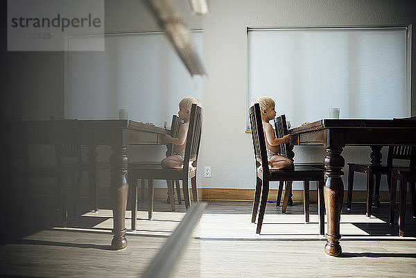 Seitenansicht eines Jungen ohne Hemd  der zu Hause auf einem Stuhl neben einem Tisch kniet