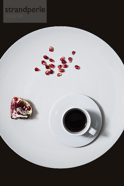 Draufsicht auf Kaffee und Granatapfel in Teller über schwarzem Hintergrund
