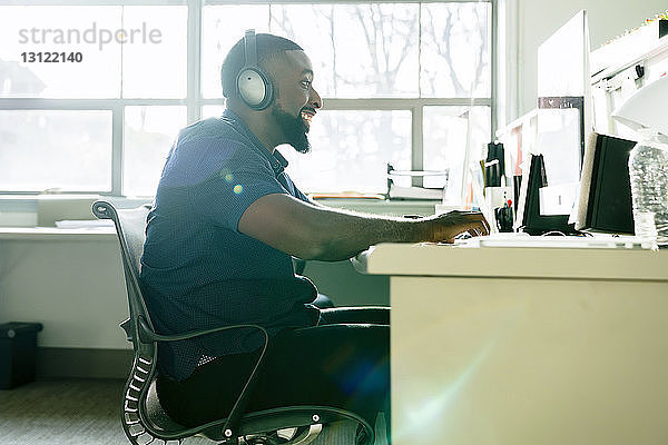 Seitenansicht eines lächelnden Geschäftsmannes  der einen Desktop-Computer benutzt  während er am Schreibtisch im Büro arbeitet