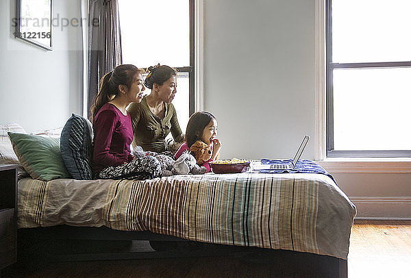 Familie schaut zu Hause auf dem Laptop im Bett einen Film an