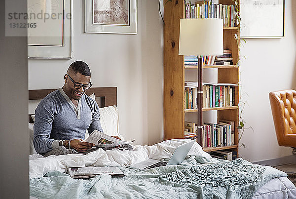 Mann liest Zeitung  während er zu Hause auf dem Bett sitzt