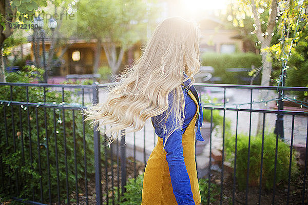 Frau mit blonden Haaren geht am sonnigen Tag am Park am Zaun vorbei