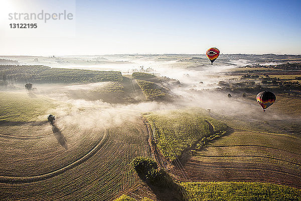 Luftaufnahme von Heißluftballons  die bei sonnigem Wetter über die Landschaft gegen den Himmel fliegen