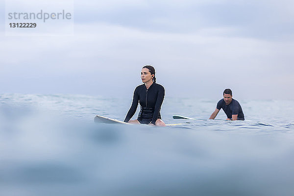 Freunde sitzen auf einem Surfbrett im Meer gegen den Himmel