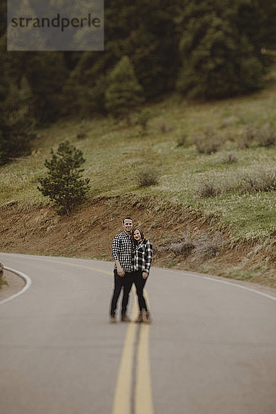 Junges Paar in voller Länge trägt kariert gemusterte Hemden  während es auf einer Landstraße steht