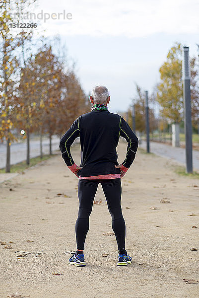 Rückansicht eines älteren Mannes mit Händen auf den Hüften  der im Herbst im Park trainiert