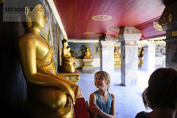 Lächelndes Mädchen betrachtet Buddhastatue im Tempel