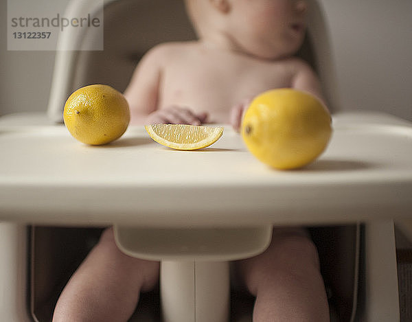 Kleiner Junge ohne Hemd auf Hochstuhl sitzend mit Zitronen im Vordergrund