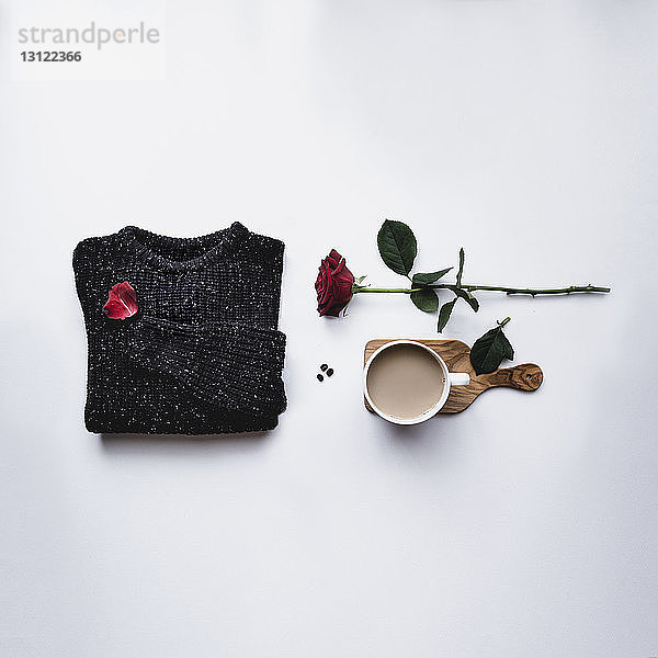 Draufsicht auf schwarzen Pullover mit Kaffee und Rose vor weißem Hintergrund
