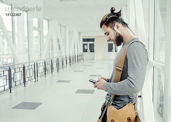 Seitenansicht eines Mannes  der ein Mobiltelefon benutzt  während er im Korridor steht
