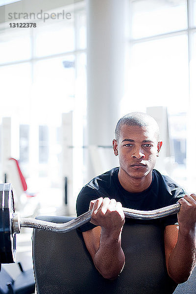 Porträt eines entschlossenen jungen Mannes beim Hanteln im Fitnessstudio
