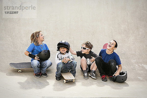 Fröhliche Jungen unterhalten sich  während sie auf der Skateboard-Rampe sitzen