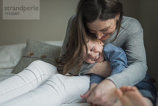 Glückliche Mutter spielt zu Hause mit ihrem Sohn im Schlafzimmer