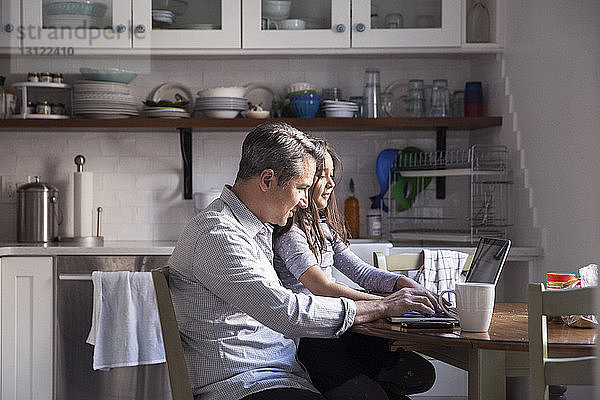 Tochter sitzt mit dem Vater am Laptop in der Küche zu Hause
