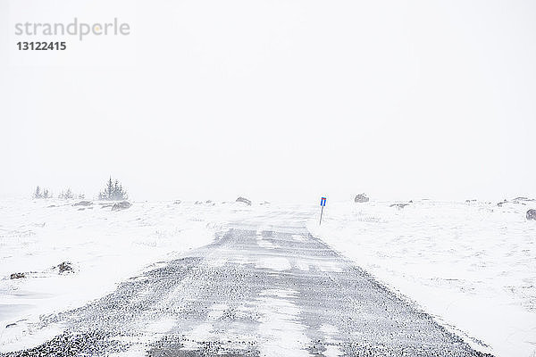 Straße inmitten eines schneebedeckten Feldes gegen klaren Himmel