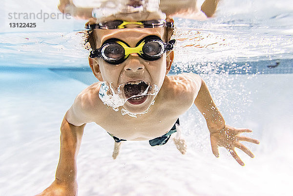 Porträt eines Jungen ohne Hemd mit offenem Mund beim Schwimmen im Schwimmbad