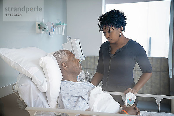 Vater spricht mit Tochter  während er im Bett auf der Krankenstation liegt und durch das Fenster gesehen wird