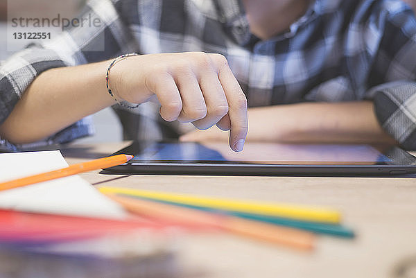Ausgeschnittene Hand eines Jungen  der auf einem Tablet-Computer bei Tisch zeichnet
