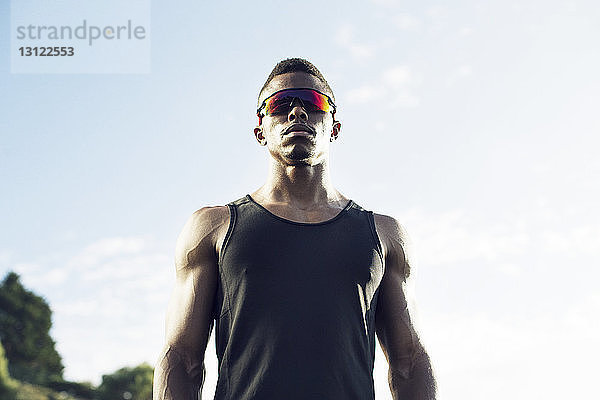 Niedriger Blickwinkel eines selbstbewussten Sportlers mit Sonnenbrille gegen den Himmel