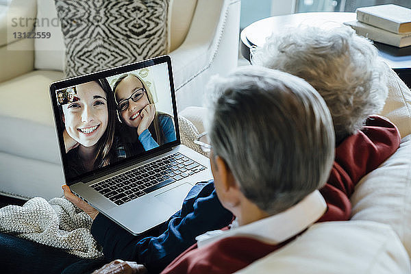 Videokonferenz eines älteren Ehepaares mit Enkelinnen über einen Laptop zu Hause