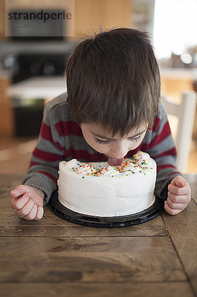 Junge leckt Sahne auf Kuchen  während er am Tisch sitzt