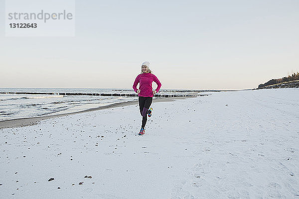 Glückliche Teenagerin joggt am Strand vor klarem Himmel