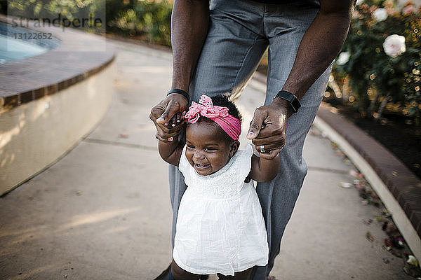 Mitschnitt eines Vaters  der seiner Tochter beim Gehen auf einem Fußweg im Park hilft
