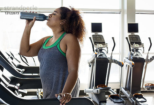 Frau trinkt Wasser  während sie im Fitnessstudio auf dem Laufband steht