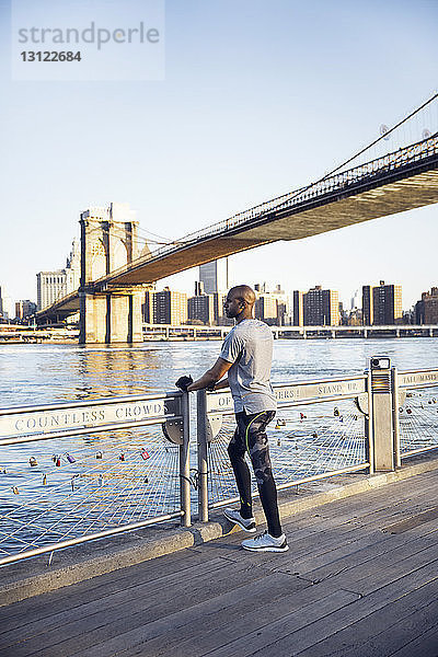Männlicher Athlet in voller Länge auf der Promenade stehend mit der Brooklyn Bridge im Hintergrund