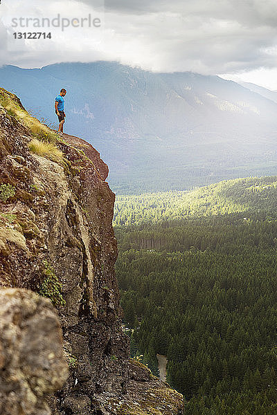 Seitenansicht eines Mannes  der auf einer Klippe gegen einen Berg steht