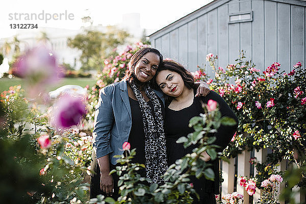 Porträt von glücklichen Schwestern  die inmitten von Pflanzen im Park stehen