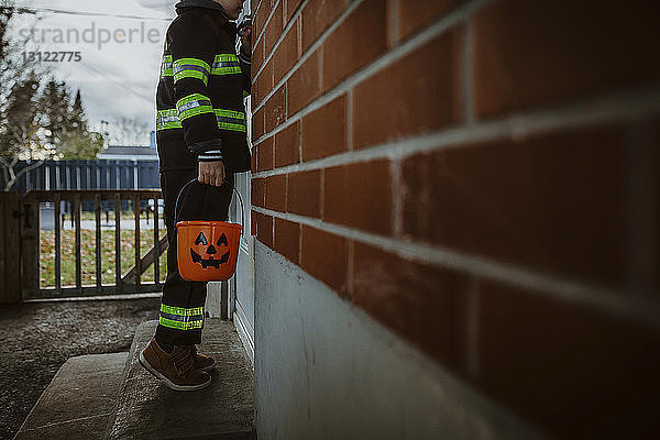 Niedriger Teil eines Jungen  der einen Halloween-Eimer hält  während er an der Tür steht