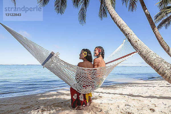 Freundinnen entspannen sich in der Hängematte am Strand vor blauem Himmel