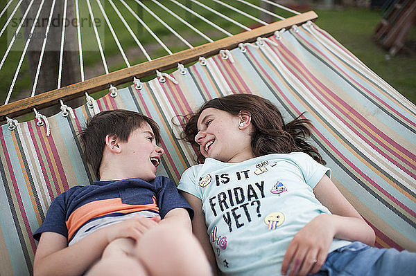 Hoher Blickwinkel auf glückliche Geschwister  die sich unterhalten  während sie sich auf der Hängematte im Hof entspannen