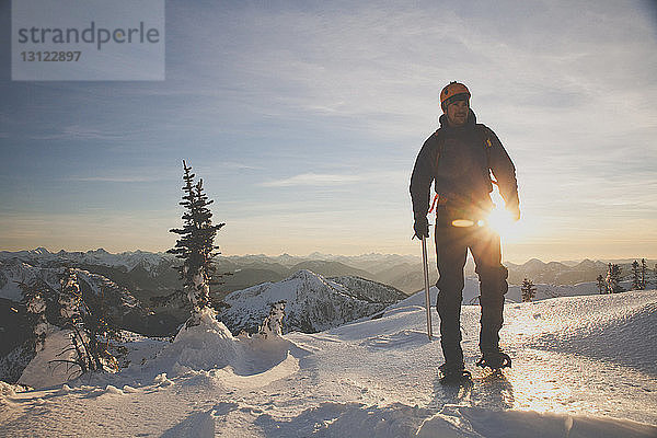 Wanderer in voller Länge mit Eispickel beim Bergsteigen auf schneebedeckten Bergen gegen den Himmel bei Sonnenuntergang