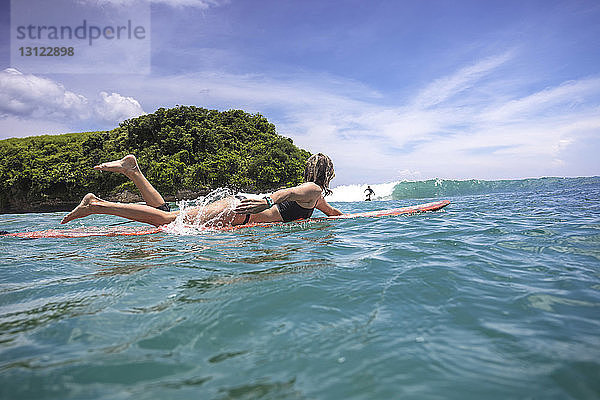 Freunde surfen auf dem Meer gegen den Himmel in Bali