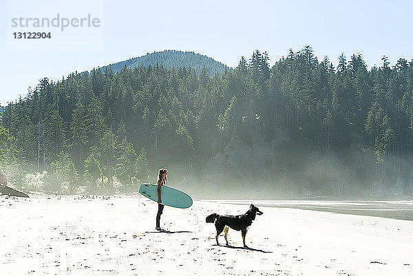 Frau hält Surfbrett mit Hund am Kanonenstrand