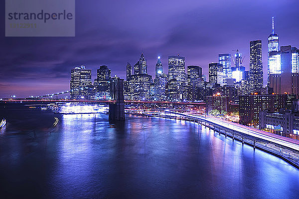 Brooklyn-Brücke über den Fluss gegen die beleuchtete Stadt