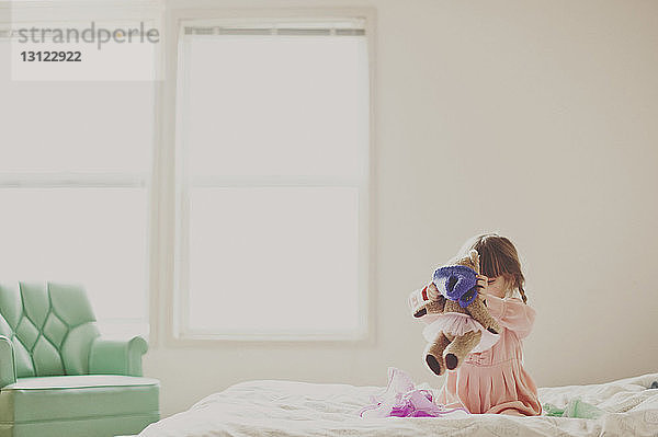 Mädchen spielt mit Teddybär im Schlafzimmer zu Hause
