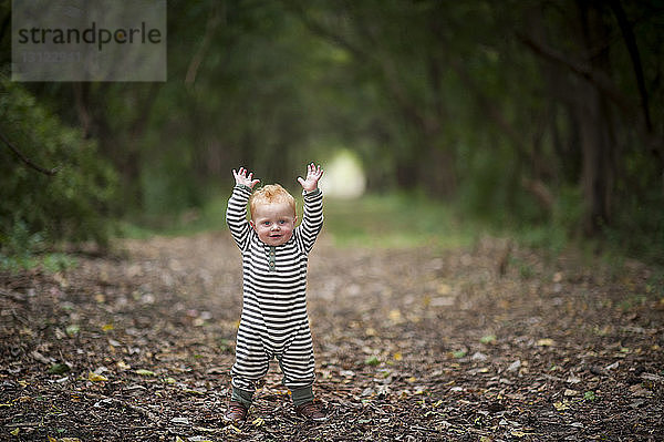 Porträt eines süßen kleinen Jungen mit erhobenen Armen im Park