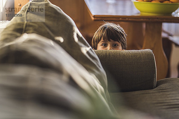 Porträt eines süßen Jungen  der sich zu Hause hinter einem Sofa versteckt