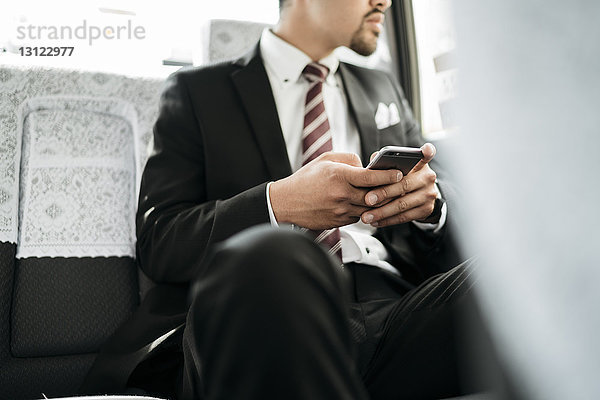 Mittelteil eines Geschäftsmannes  der ein Smartphone in der Hand hält  während er im Taxi sitzt