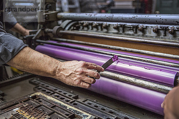 Mann trägt in Workshop violette Farbe auf Druckwalze auf