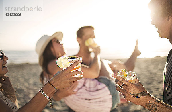 Freunde halten Getränke in der Hand  während sie am Strand genießen