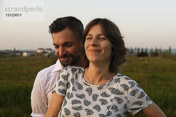 Mann umarmt PRegnant Frau  während er auf dem Feld vor klarem Himmel steht