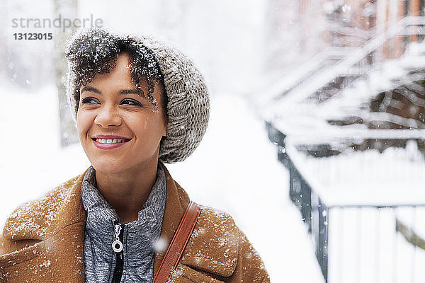 Lächelnde Frau schaut weg  während sie bei Schneefall auf schneebedecktem Feld geht