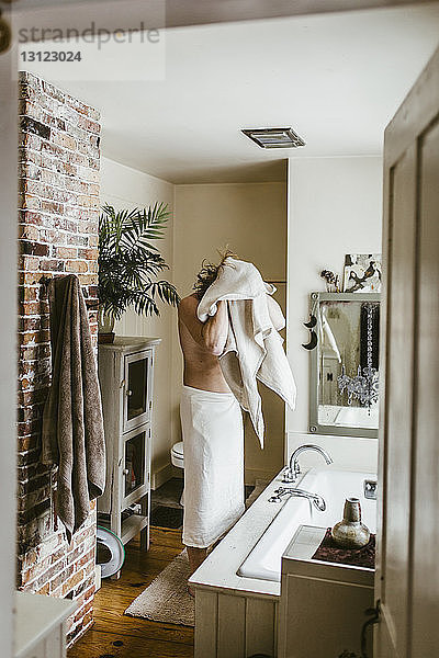 Mann ohne Hemd  der die Haare mit einem Handtuch trocknet  während er im Badezimmer steht  durch die Tür gesehen
